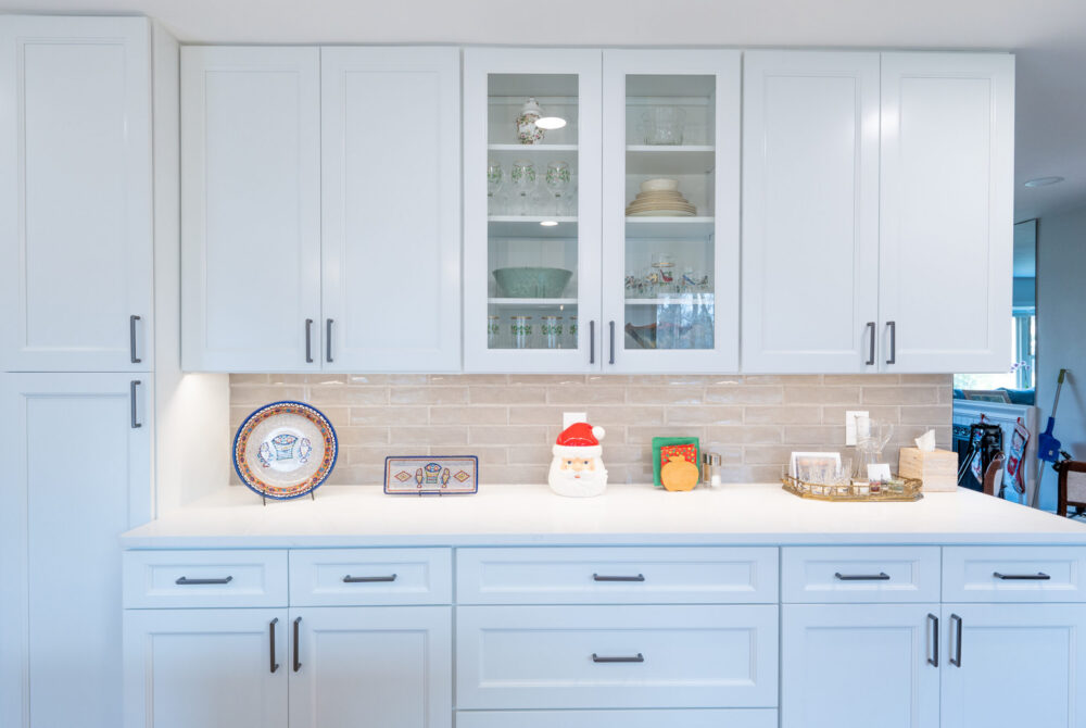 white kitchen cabinets with glass display doors and beige subway tile backsplash under cabinet lighting