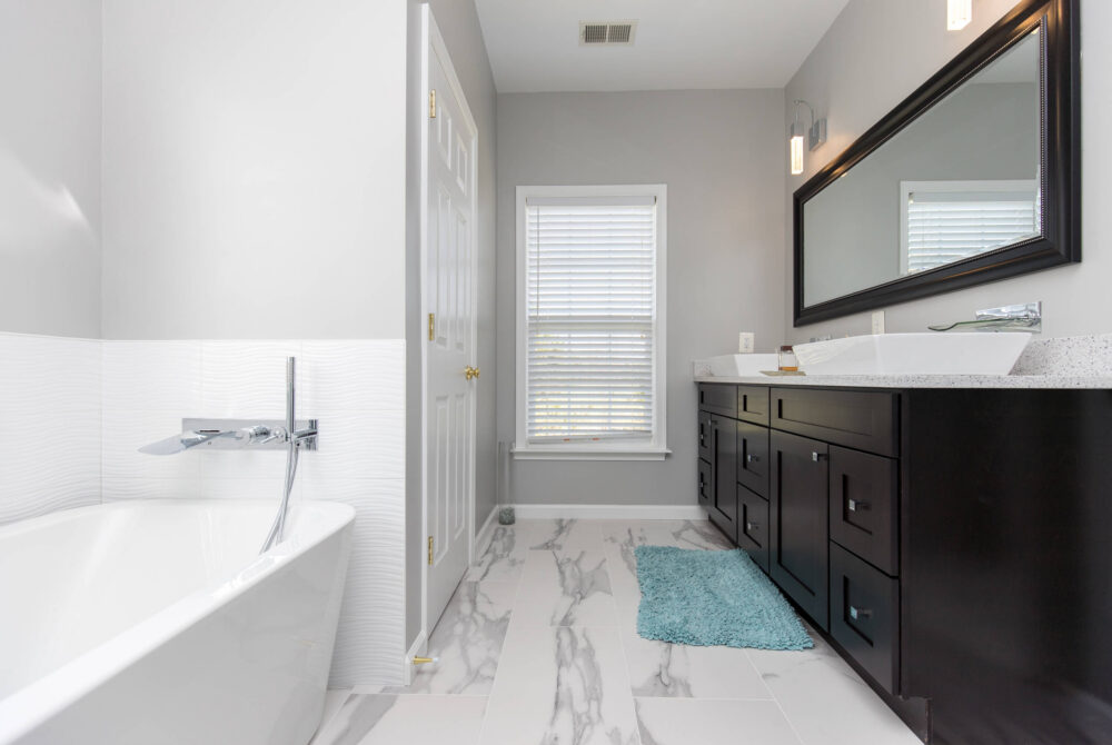 modern bathroom remodel with freestanding tub, marble tile floor, dark wood vanity, and large wall mirror