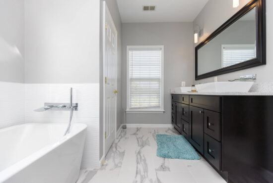 modern bathroom remodel with freestanding tub, marble tile floor, dark wood vanity, and large wall mirror