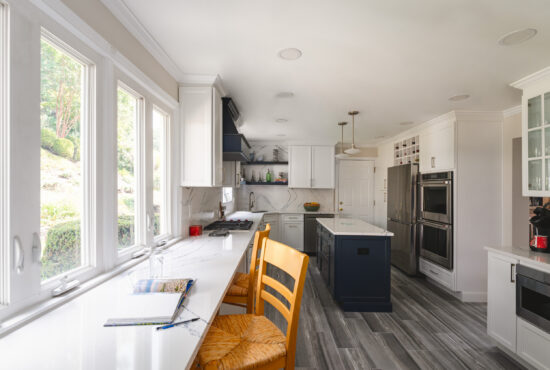 A long galley kitchen remodel featuring white cabinetry, marble-veined quartz countertops, and a unique breakfast bar seating area along a large window.