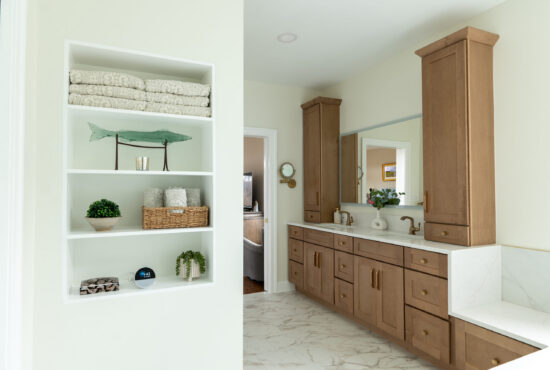 A luxury bathroom remodel featuring a long natural oak double vanity with gold hardware and a custom white built-in linen storage shelving unit.