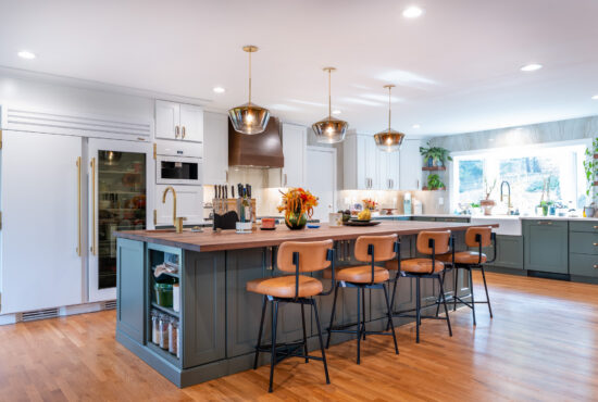 High-end kitchen remodel in Cascades, Sterling, VA with a sage green island, a butcher block walnut countertop, brass pendant lights, and a panel-front refrigerator.