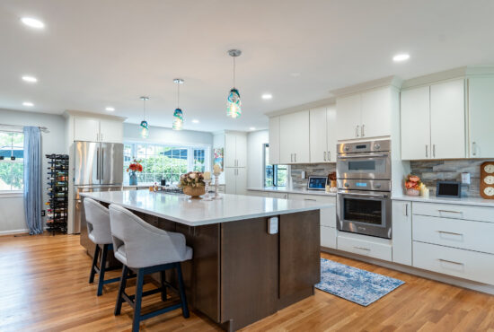 Contemporary kitchen in Vienna, VA, with white cabinets, a dark wood island, upholstered seating, and blue glass pendant lights.