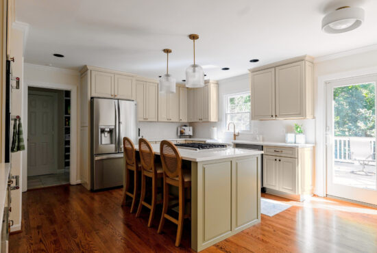 Kitchen with cream cabinets, a sage green island, three cane-back stools, and glass pendant lights beside sliding patio doors.