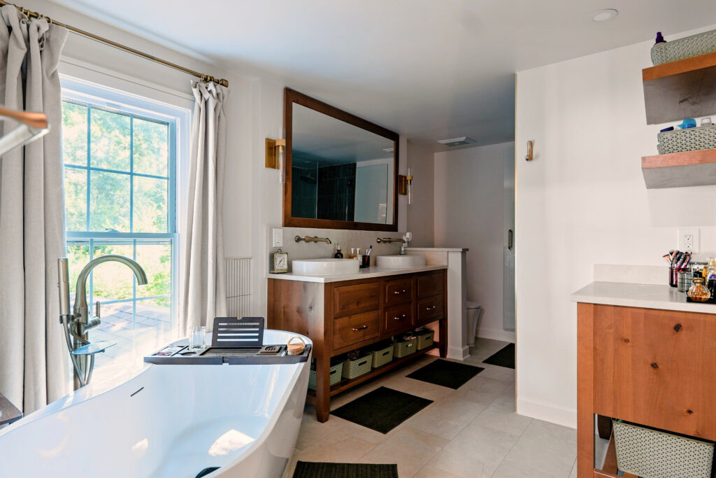Wide bathroom view with a freestanding tub beneath the window, a wood double vanity, and a matching storage cabinet.