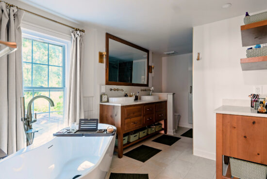 Wide bathroom view with a freestanding tub beneath the window, a wood double vanity, and a matching storage cabinet.